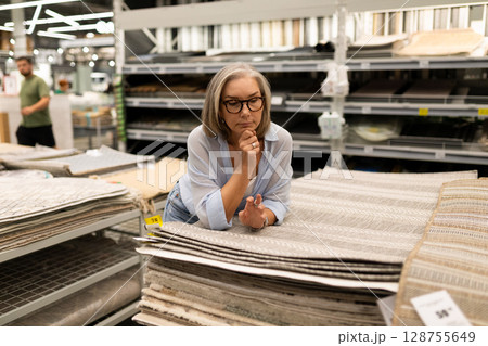 Woman thoughtfully selecting home decor items in a retail store while shopping in a hypermarket Woman thoughtfully selecting home decor items in a retail store while shopping in a hypermarket 128755649