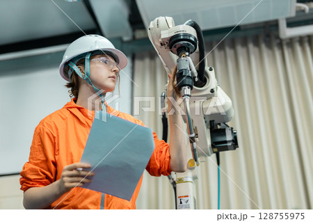 women echnician maintenance checking hardware robotic arm system of automation machine in factory. Service programming machinery welding robots in production at factory industry. women echnician maintenance checking hardware robotic arm system of automation machine in factory. Service programming machinery welding robots in production at factory industry. 128755975