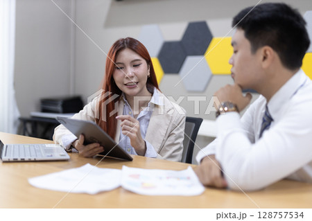 Colleagues collaborate over financial documents, pointing out key figures and charts in a contemporary office environment, enhancing teamwork and communication. 128757534