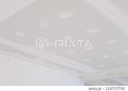 Smooth gypsum board ceiling edges seen during interior renovation phase. Electrical wire installation in progress. Plastering process prepares building structure ceilings ready for finish Smooth gypsum board ceiling edges seen during interior renovation phase. Electrical wire installation in progress. Plastering process prepares building structure ceilings ready for finish 128757708