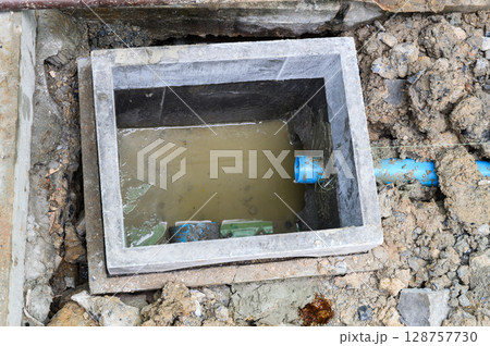 Problematic open concrete drain pit with dirty water during messy house renovation. damaged septic system or plumbing awaiting repair underground with blue PVC pipe Problematic open concrete drain pit with dirty water during messy house renovation. damaged septic system or plumbing awaiting repair underground with blue PVC pipe 128757730