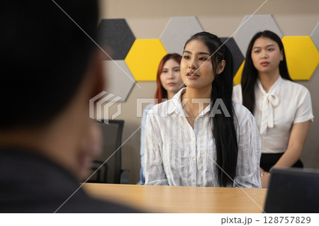 Sleek office with contemporary design, a young woman speaks confidently while presenting her thoughts. Two attentive colleagues listen closely, emphasizing teamwork and professional engagement. 128757829