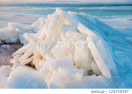 Frozen shoreline with stacked ice slabs at sunset, creating a surreal winter landscape of broken crystalline layers. 128758397