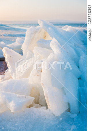 Frozen ocean shoreline with stacked ice slabs on sunset, winter landscape of broken crystalline layers. 128758398