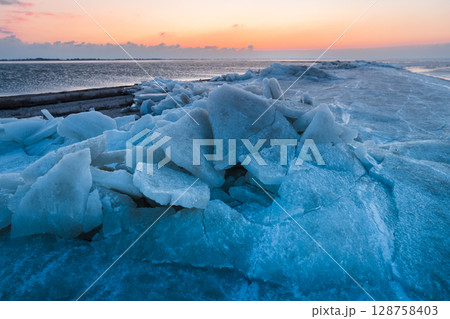 Frozen sea with stacked ice slabs at sunset, creating a winter landscape of broken crystalline layers. 128758403