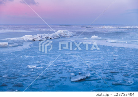 Frozen sea with cracked ice and stacked slabs under a pastel pink and blue sunset sky in winter stillness. 128758404