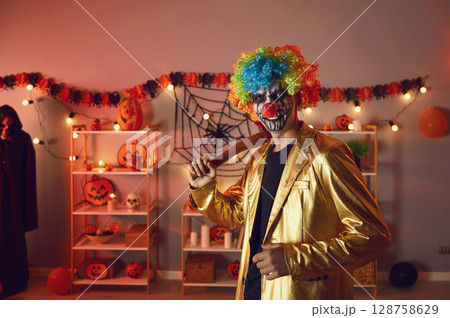 Portrait of adult man dressed up as creepy evil clown with axe at Halloween party Portrait of adult man dressed up as creepy evil clown with axe at Halloween party 128758629