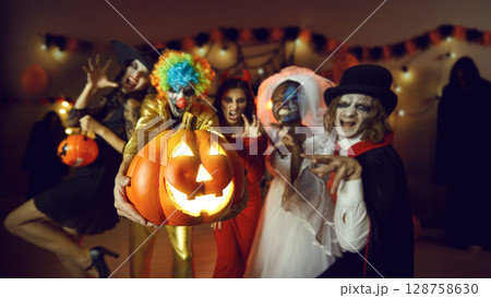 Group of adult friends with a jack-o-lantern having fun at a costume party at home Group of adult friends with a jack-o-lantern having fun at a costume party at home 128758630