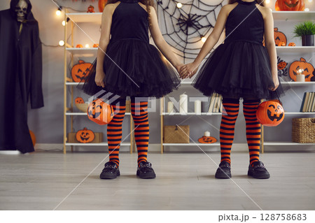 Two kids dressed up for Halloween go trick or treating with orange pumpkin baskets 128758683