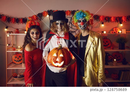 Portrait of cheerful adult friends with glowing jack-o-lantern in hands at Halloween party. 128758689
