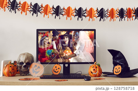 Computer with Halloween party themed desktop background standing on decorated desk 128758718