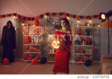 Young woman who's dressed in costume of evil devil holding Halloween jack-o-lantern 128758738