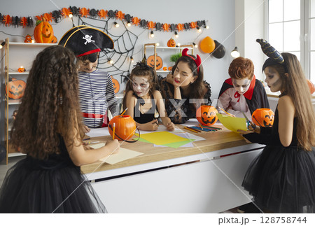 Group of children together with woman prepares handmade Halloween decorations from paper. 128758744