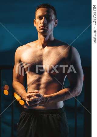 Muscular athlete posing powerfully at night, strength and dedication, Toned man with perfect body displaying power and discipline in evening silhouette 128758784