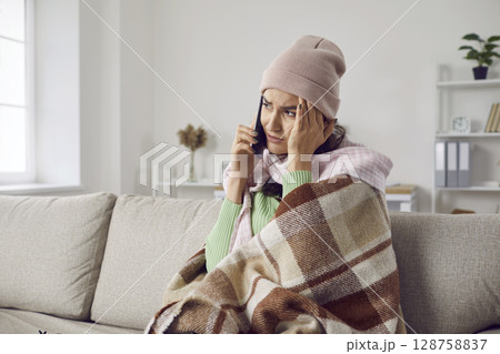 Unhappy and exhausted woman with cold symptoms sitting at home calls her doctor or ambulance. Unhappy and exhausted woman with cold symptoms sitting at home calls her doctor or ambulance. 128758837