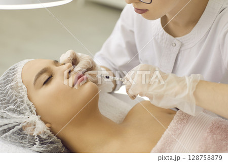 Woman receiving injection for plumper lips at clinic of aesthetic medicine 128758879