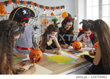 Arts and Crafts teacher and children dressed up in costumes having fun class on Halloween 128758902
