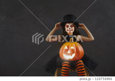 Girl with Halloween skull makeup and Jack-o-lantern on dark copy space background Girl with Halloween skull makeup and Jack-o-lantern on dark copy space background 128758960