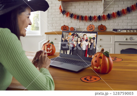 Happy woman in front of computer screen having online Halloween party with children Happy woman in front of computer screen having online Halloween party with children 128759003