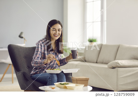 Happy woman drinking coffee and eating vegetable salad from takeout meal delivery Happy woman drinking coffee and eating vegetable salad from takeout meal delivery 128759009