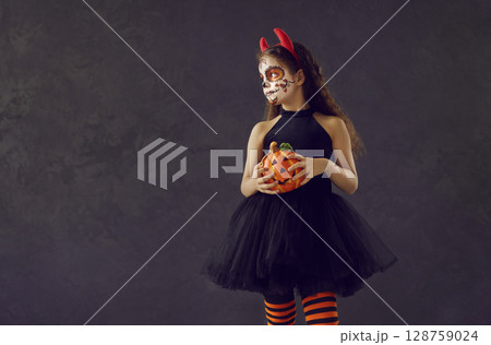 Portrait of girl with Halloween skull makeup standing on dark copy space background Portrait of girl with Halloween skull makeup standing on dark copy space background 128759024
