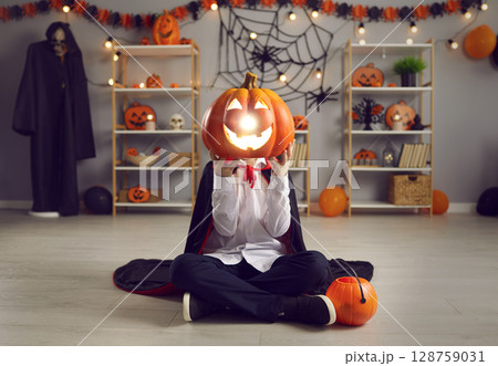 Kid with a Jack-o-lantern head having fun at a Halloween fancy dress party at home 128759031