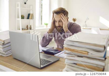 Tired exhausted male office worker working all day on financial report counting figures. 128759044
