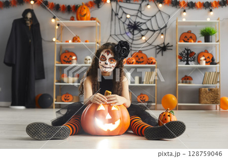 Portrait of cute little girl in Halloween costume sitting on floor with jack-o-lantern. Portrait of cute little girl in Halloween costume sitting on floor with jack-o-lantern. 128759046