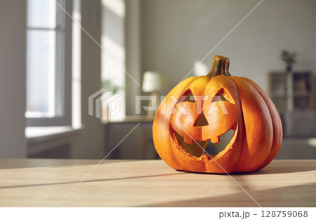 Festive Halloween background with a cute smiley Jack-O-lantern on a table at home Festive Halloween background with a cute smiley Jack-O-lantern on a table at home 128759068
