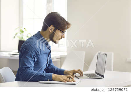 Millennial man work online on laptop in office Millennial man work online on laptop in office 128759071