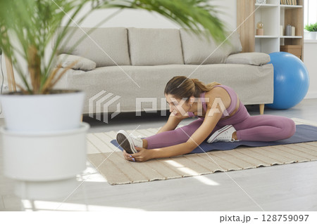 Fit young woman doing leg stretching exercise during her fitness workout at home 128759097
