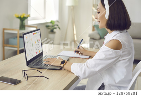 Woman sitting in front of laptop at home, studying online business course and taking notes Woman sitting in front of laptop at home, studying online business course and taking notes 128759281