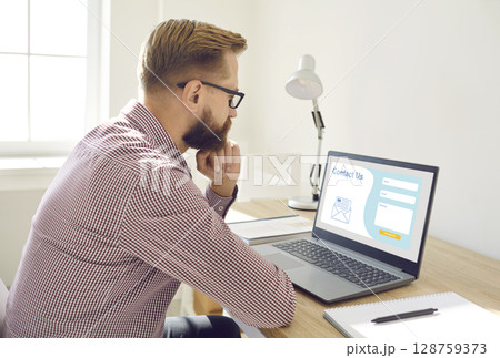 Man sitting and thinking what to write in Contact Us form on landing page website 128759373