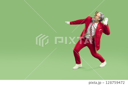 Horizontal shot of joyful man dressed in red suit like Santa Claus, dances and has fun 128759472
