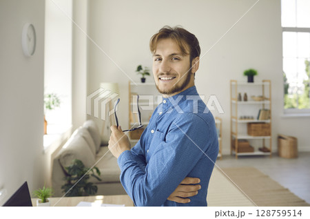 Portrait of handsome young business man standing confidently in office in front of camera. 128759514