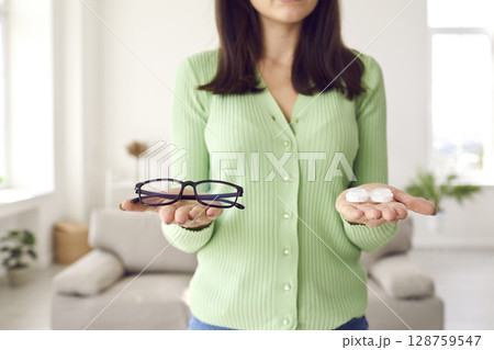 Young woman is holding glasses and eye lenses and trying to choose which to wear 128759547