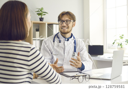 Young male doctor tells and explains to female patient her diagnosis during consultation at clinic. Young male doctor tells and explains to female patient her diagnosis during consultation at clinic. 128759581