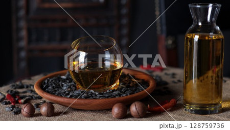Warm oil in a glass bowl surrounded by spices and nuts on a textured surface 128759736