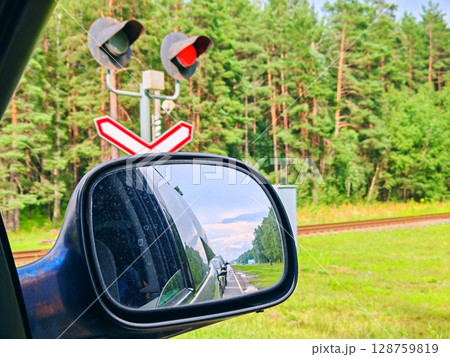 red light on the railway in front of the train. Cars waiting in front of a railroad crossing with a red light while a train crosses the road red light on the railway in front of the train. Cars waiting in front of a railroad crossing with a red light while a train crosses the road 128759819