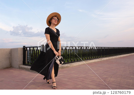 Fashionable woman walks with handbag on riverside promenade Fashionable woman walks with handbag on riverside promenade 128760179
