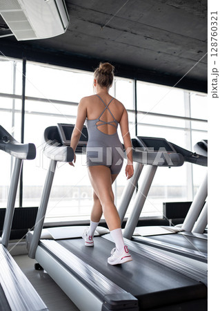 A fit woman confidently walking on a treadmill in a bright and inviting gym, promoting fitness and overall health. 128760321
