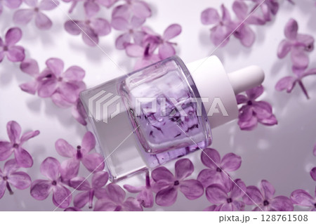 A bottle of serum with petals in water with lilac flowers. 128761508