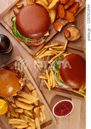 Delicious hamburgers with french fries, nuggets and sauces served on wooden boards Delicious hamburgers with french fries, nuggets and sauces served on wooden boards 128761894