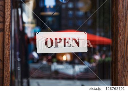 Open Sign on Storefront Glass with Blurred City Street and Outdoor Cafe Reflections 128762391