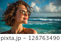 Happy Woman with Curly Hair and Sunglasses on a Sunny Beach 128763490