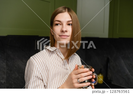 Young woman holding glass cup of coffee in modern kitchen. Young woman holding glass cup of coffee in modern kitchen. 128763561