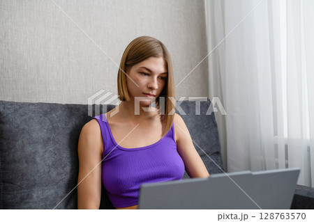 Focused young woman working on laptop at home on sofa. 128763570