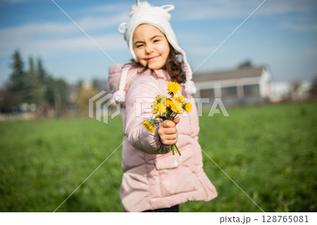 bouquet of dandelions in hand of small smiling girl in warm clothes bouquet of dandelions in hand of small smiling girl in warm clothes 128765081