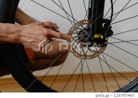 Close-up of mechanic hand pointing out worn brake disc on bicycle wheel, emphasizing significant safety hazard requiring immediate attention and maintenance. Concept of bike service. 128765465