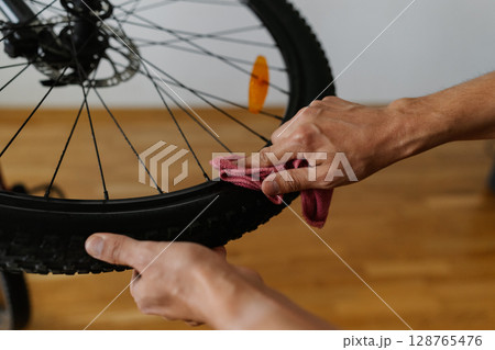 Bike mechanic cleaning tire of bicycle wheel with cloth, ensuring optimal performance and maintaining bike pristine condition in professional workshop, close-up. Concept of bike maintenance, service. 128765476